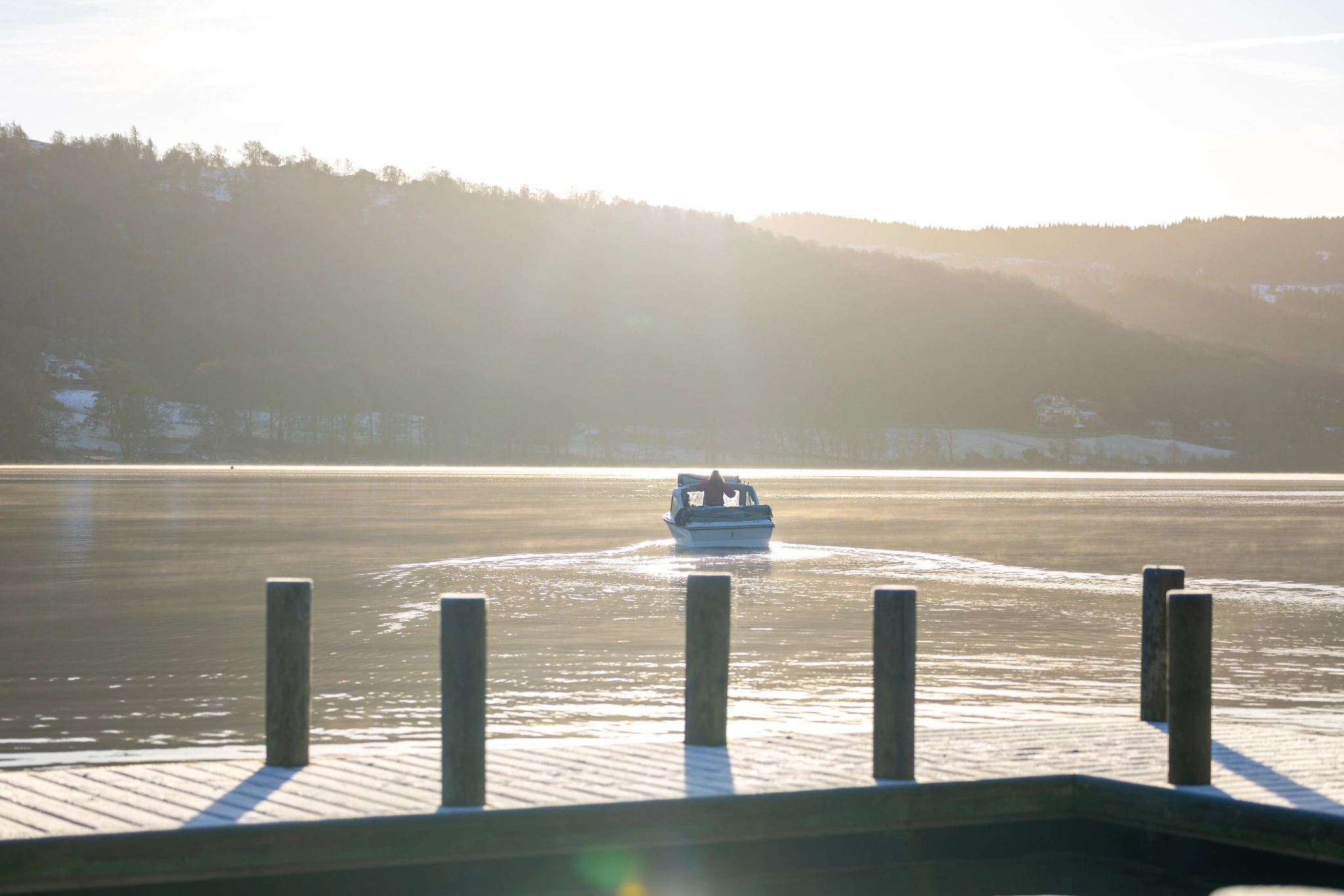 small white motor boat sailing away from a wooden jetty on a sunny winters day