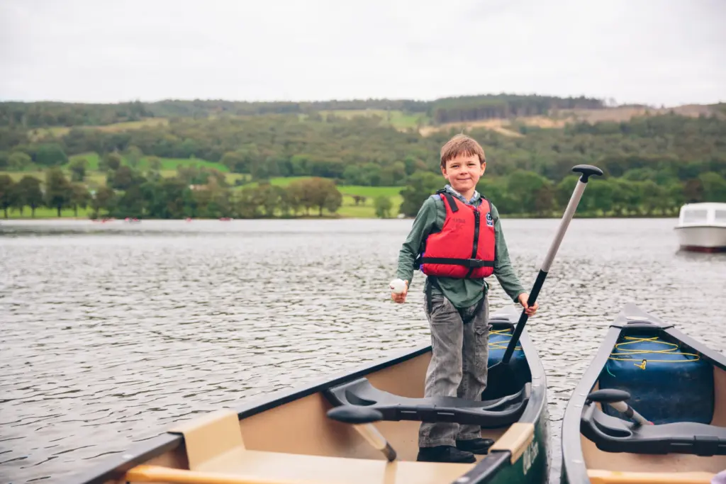 Young boy in a red buoyancy aid stood on a rowing boat