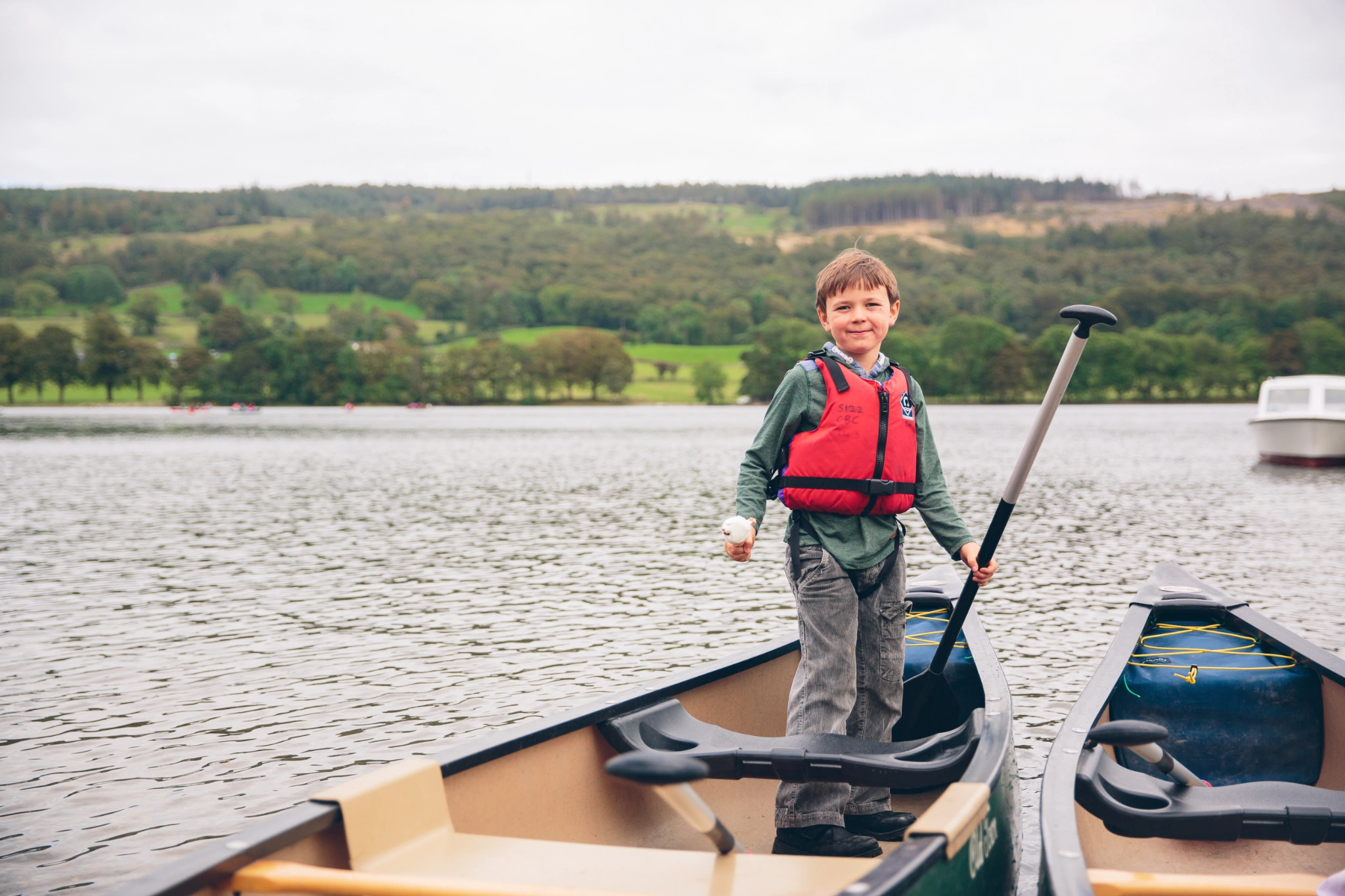 Young boy in a red buoyancy aid stood on a rowing boat