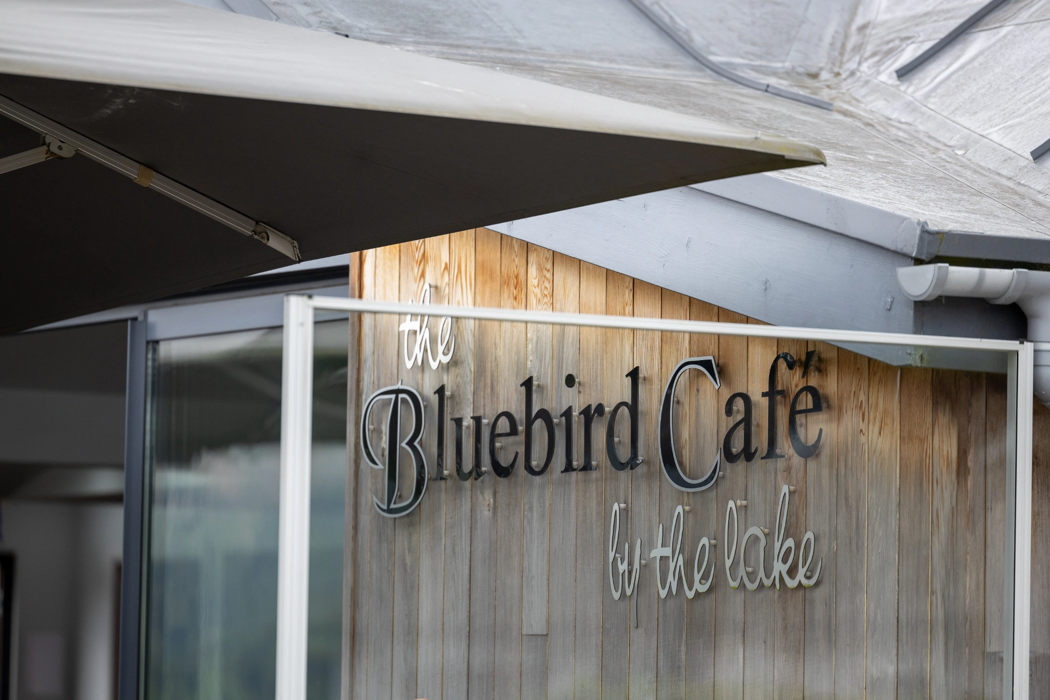 white parasol and wooden exterior of the Bluebird Cafe, with the cafe sign on the wall