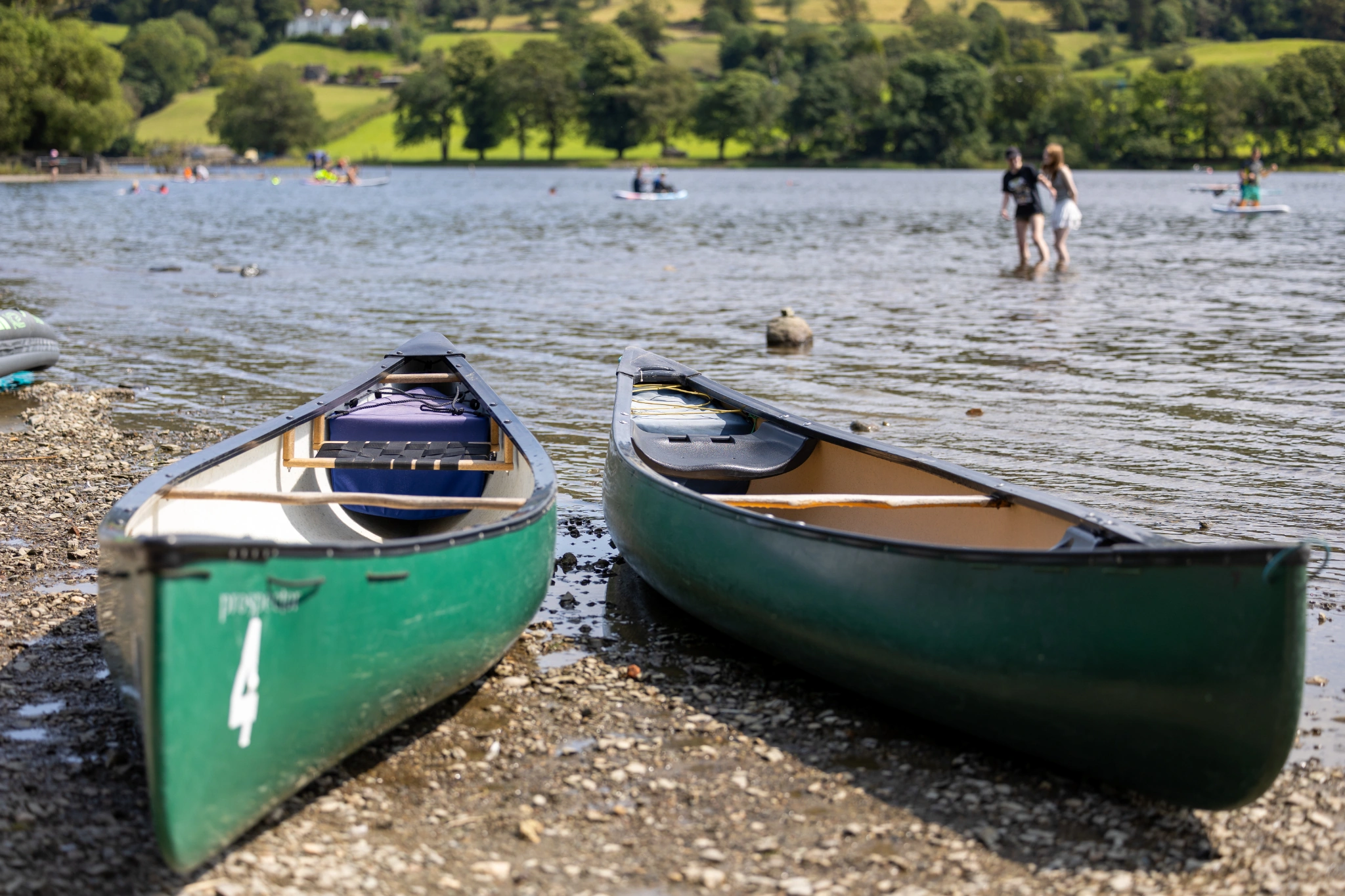 two green canoes on a lake shore with people stood in the water backdrop