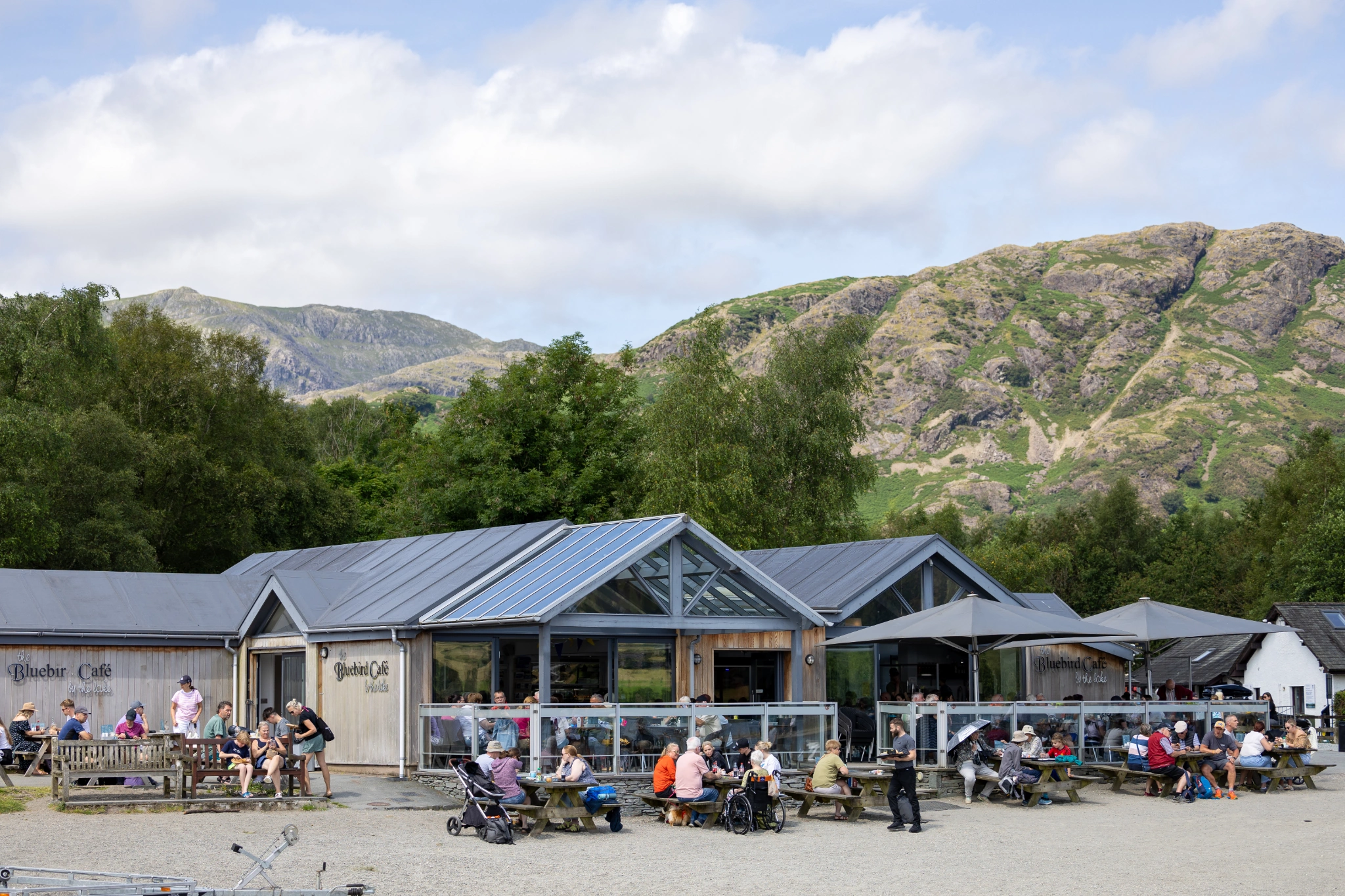 exterior view of the Bluebird Cafe on the lake shore of Coniston Water with green woodland and fells in the backdrop