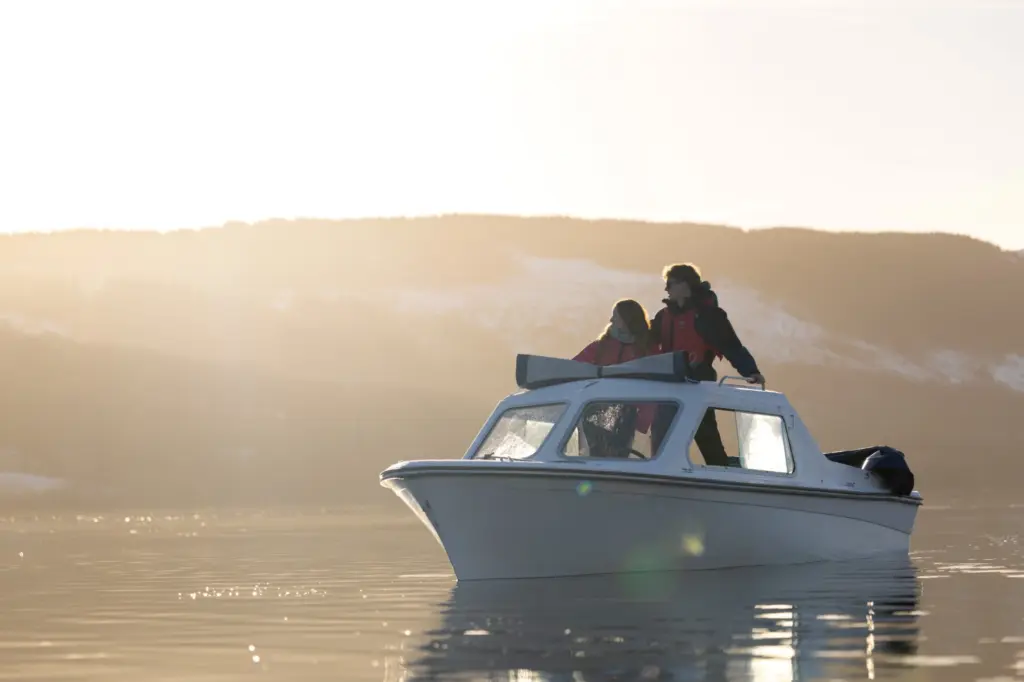two adults stood on a small, white, open top motorised boat on a sunny winters day